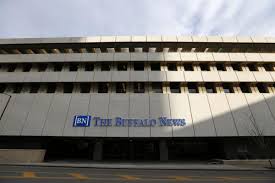 A large, modern building with The Buffalo News sign and logo on its exterior, seen from across the street under a partly cloudy sky.