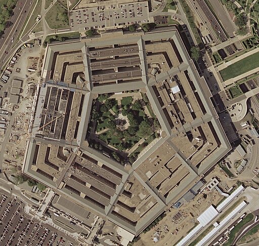 Aerial view of the Pentagon, a large five-sided building complex with an open courtyard in the center, surrounded by parking lots, roads, and greenery.