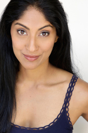 A woman with long black hair and medium skin tone smiles softly at the camera. She is wearing a navy blue sleeveless top with scalloped edges and has a neutral background behind her.