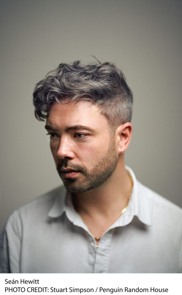 A man with short, wavy, gray hair and a neatly trimmed beard wears a light-colored, open-collar shirt. He looks slightly to the side against a soft, neutral background.