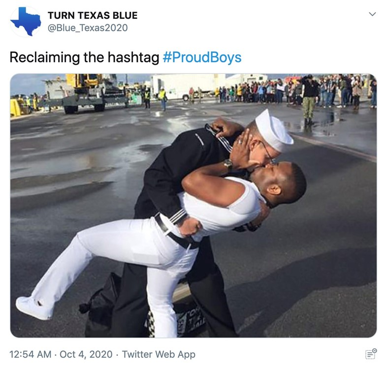 Two men in Navy uniforms passionately kiss on a dock, with one dipping the other, echoing the iconic WWII V-J Day photo. People and ships can be seen in the background. The tweet reads: Reclaiming the hashtag #ProudBoys.
