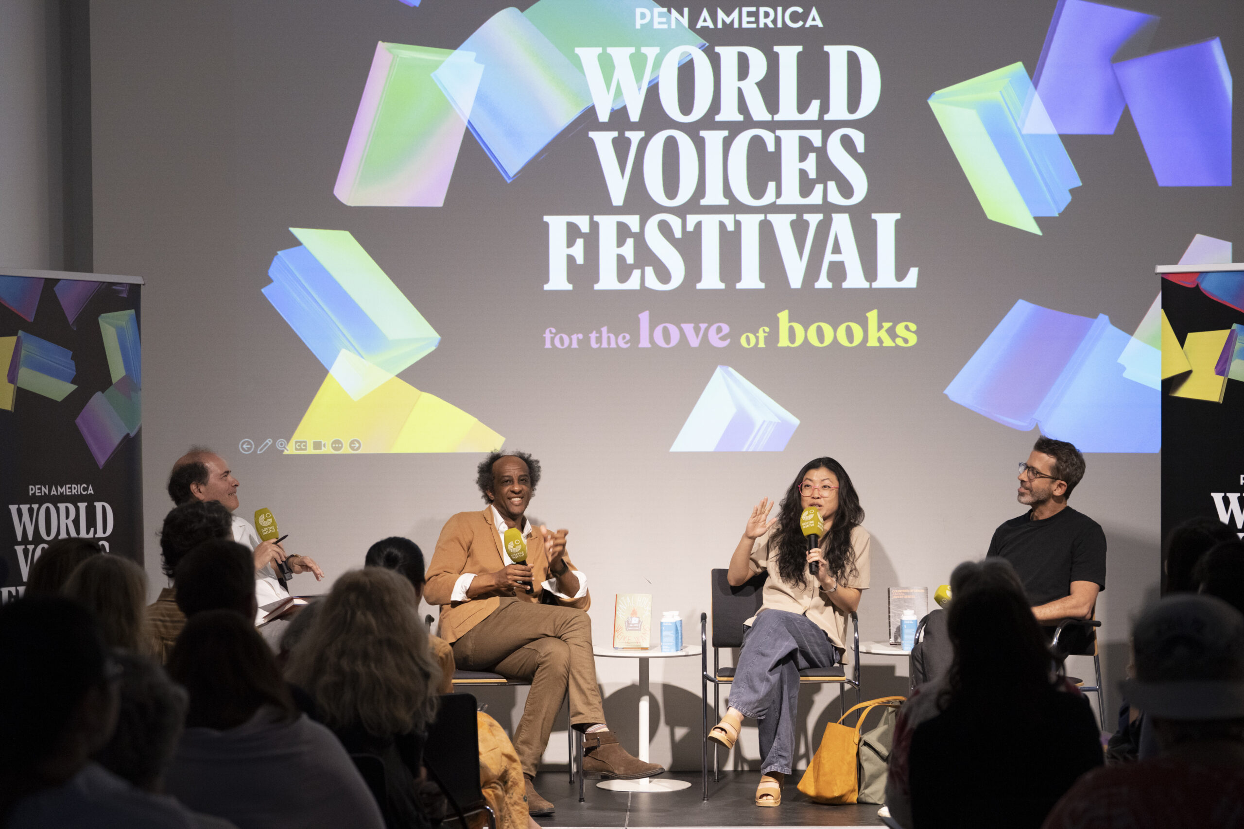 Four panelists sit on stage speaking to an audience at the PEN America World Voices Festival, with a large screen behind them displaying the festival logo and colorful book graphics.