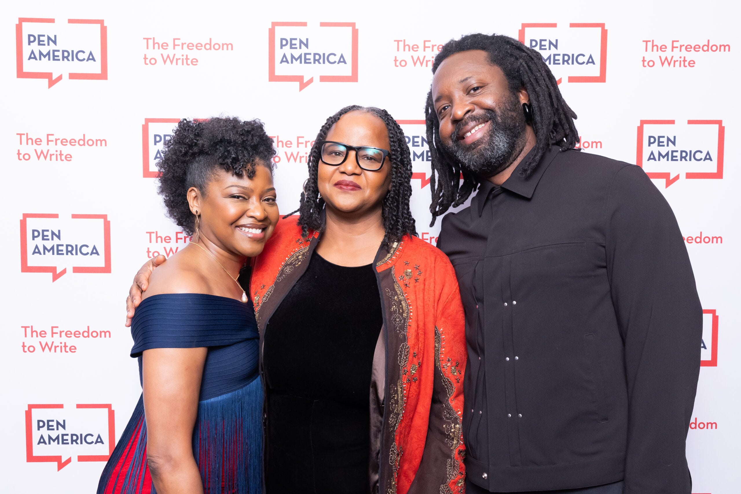 Three people stand closely together, smiling for a photo at a PEN America event. A step-and-repeat backdrop displays the PEN America logo and the slogan The Freedom to Write in red and white.