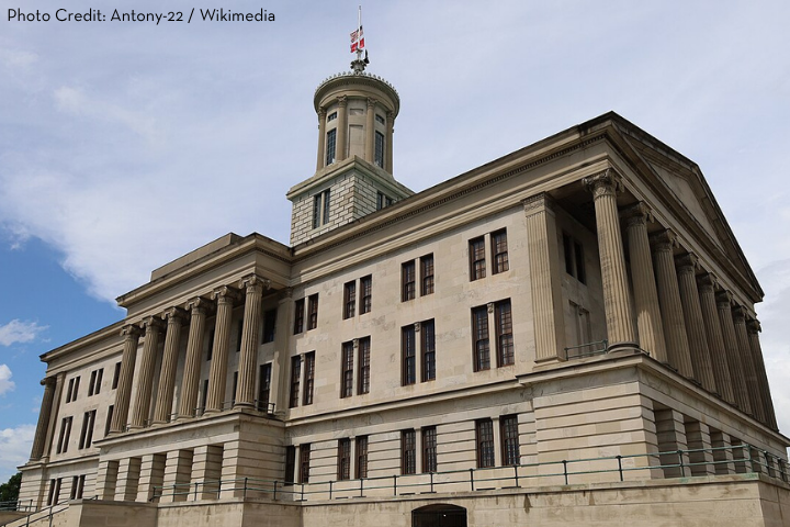 Historic government building with tall columns and a central tower topped by a flag, set against a partly cloudy sky. Photo credit: Antony-22 / Wikimedia.
