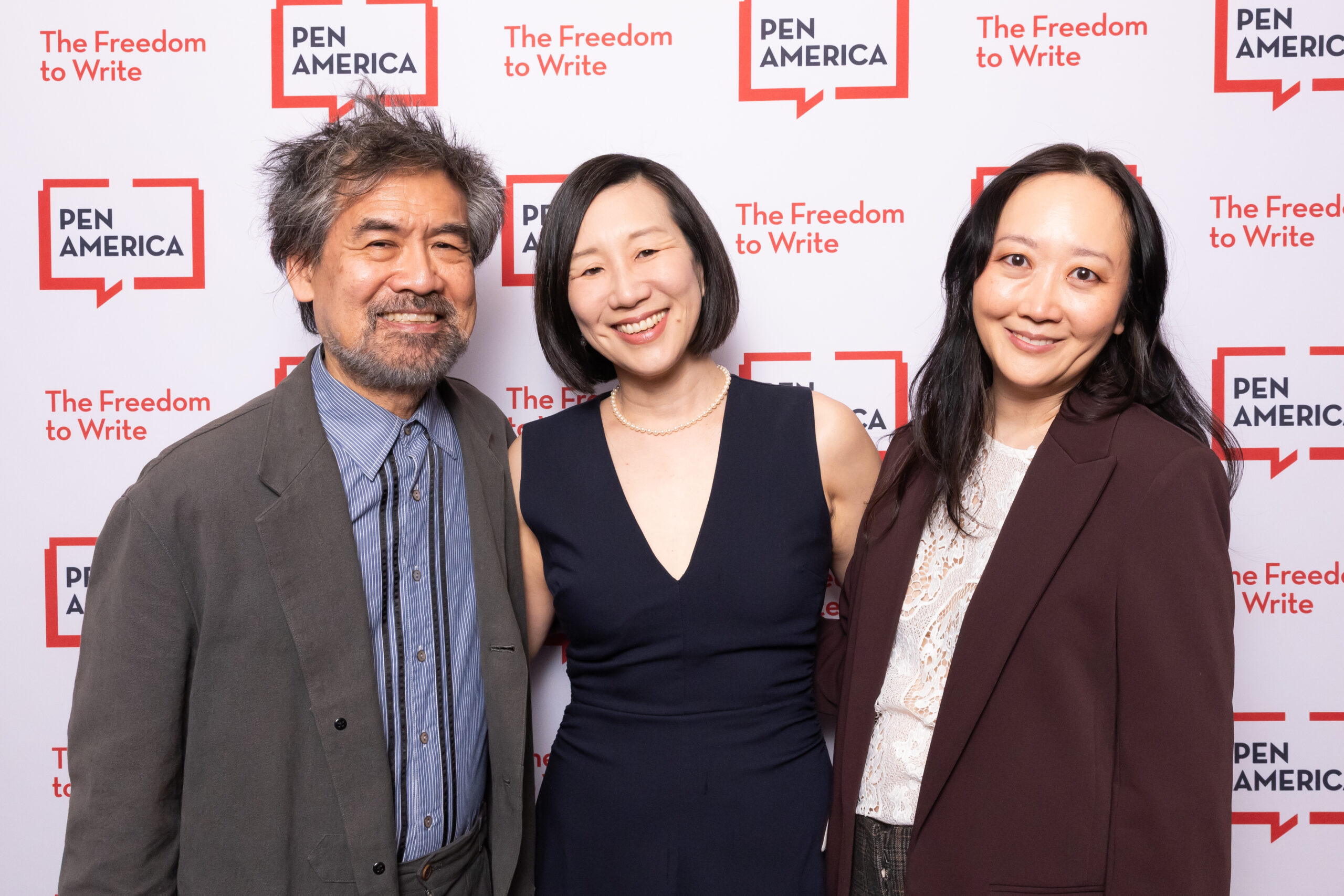 Three people smiling and posing together at a PEN America event, standing in front of a backdrop with PEN America logos and the slogan “The Freedom to Write.”.