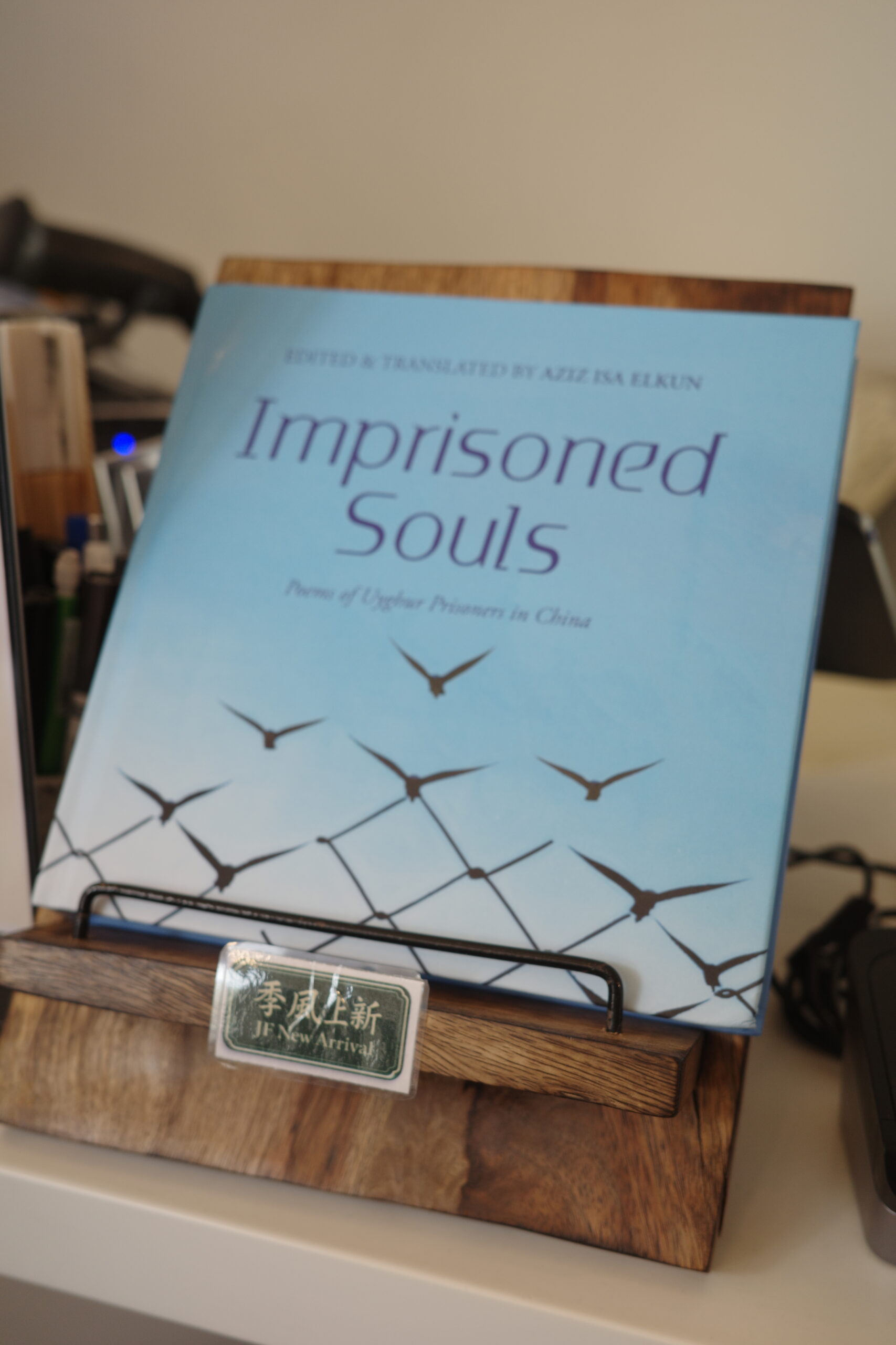 A book titled Imprisoned Souls: Poems of Uyghur Prisoners in China, edited and translated by Aziz Isa Elkun, is displayed on a wooden stand with a green label in front of it.