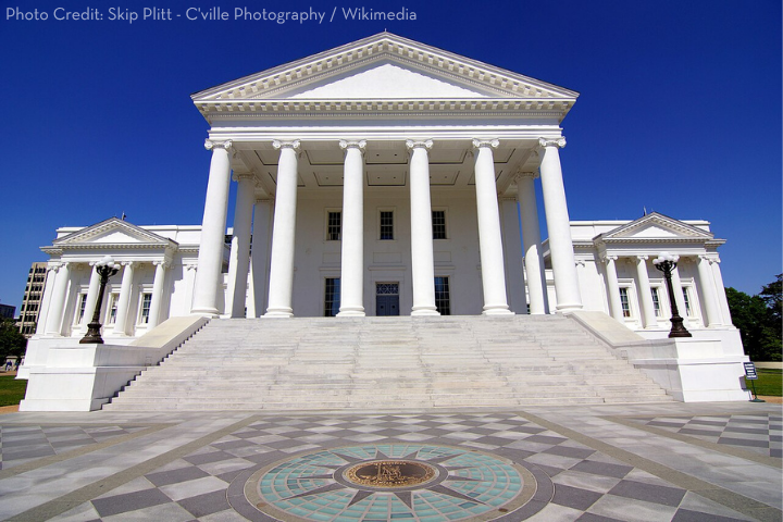 The image shows the Virginia State Capitol building, a large white neoclassical structure with tall columns and a grand staircase, set against a clear blue sky. A decorative circular pattern is visible in the foreground.