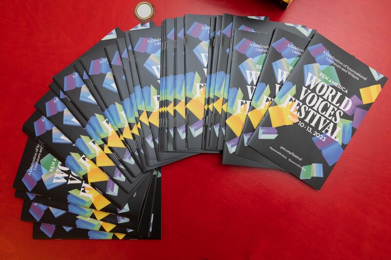 A collection of colorful pamphlets fan out on a red surface. The pamphlets are for the PEN America World Voices Festival, dated May 10-13, 2023. They feature a geometric design with bold text.