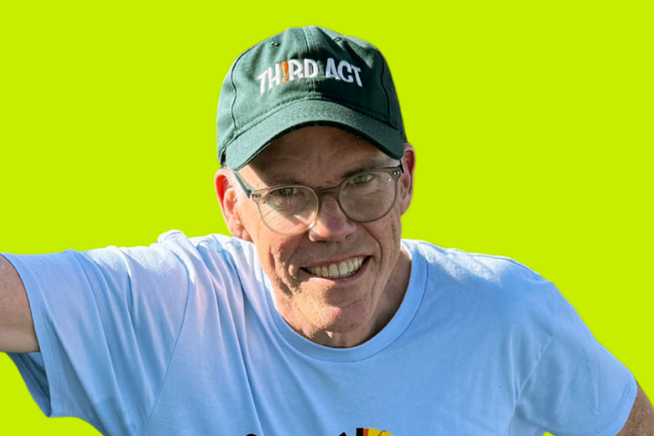 A smiling man wearing glasses, a green baseball cap that reads Third Act, and a light blue T-shirt, standing against a bright lime green background.