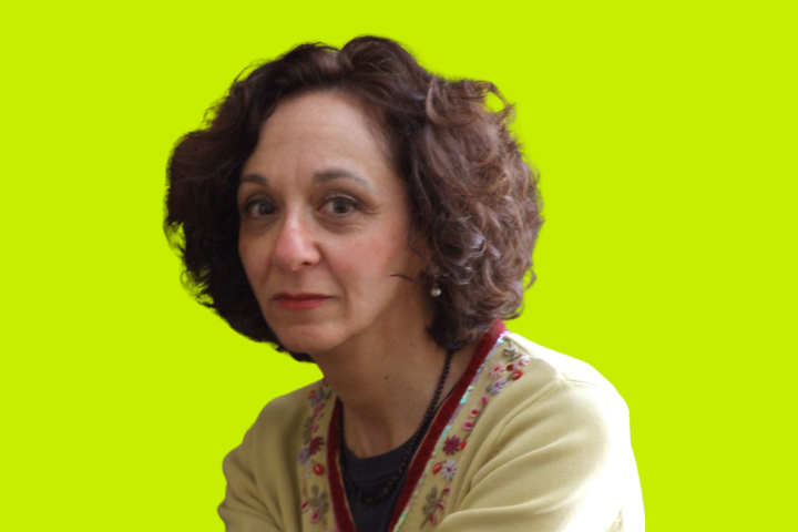 A woman with curly dark hair and light skin wearing a cream-colored sweater with floral embroidery sits against a bright yellow-green background, looking slightly to the side.