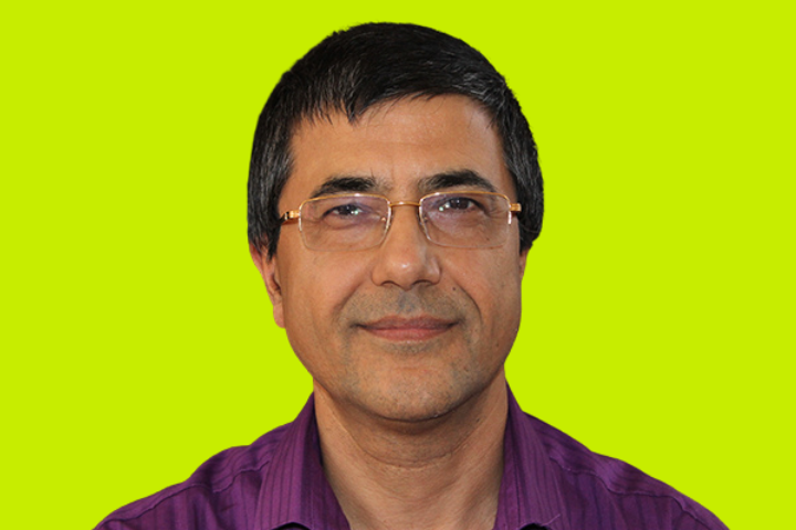 A middle-aged man with short black hair, wearing glasses and a purple collared shirt, is smiling slightly. The background is a solid bright yellow-green color.