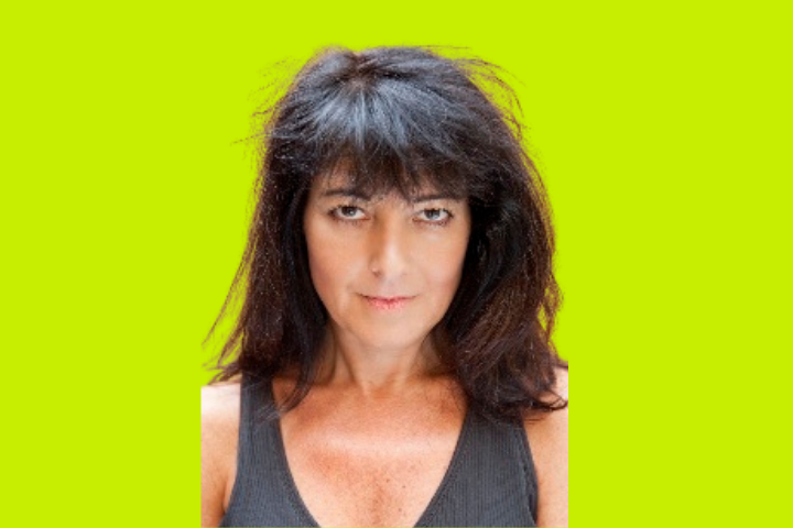 A woman with medium-length dark hair and a neutral expression wears a sleeveless gray top, posed against a bright yellow-green background.