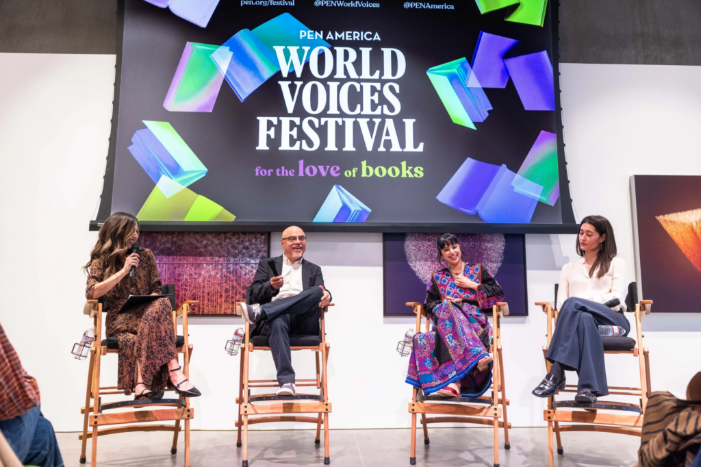 Four people sit on stage with microphones at the PEN America World Voices Festival, under a large colorful screen that reads for the love of books. The panelists appear engaged in a discussion about literature.