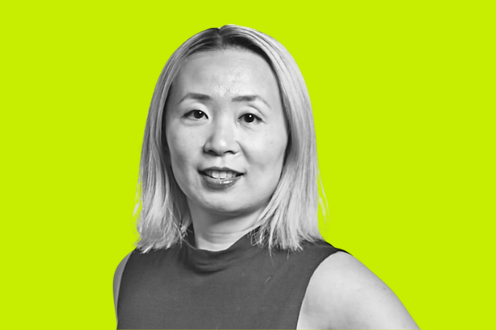 A woman with straight, shoulder-length blonde hair smiles slightly. She is wearing a sleeveless, dark-colored top. The background is a solid bright yellow-green color.